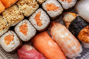 Multicolored rolls and sushi rice, caviar and salmon, eel, trout on the table in the background. Toned.