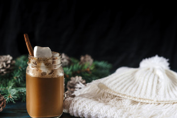 New Year's cappuccino with marshmallows, white knitting scarf on an old blue wooden table, for decoration, pine for a branch with cones
