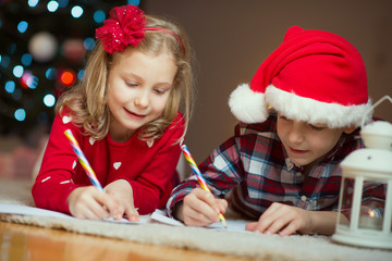 Two happy children writing letter to Santa Claus at home near New Year tree