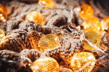 Christmas background with a glowing golden garland on a knitted brown scarf. A beautiful festive idea for postcards and posters. Concept winter Holidays