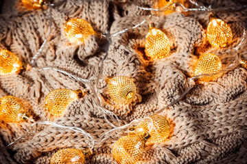 Christmas background with a glowing golden garland on a knitted brown scarf. A beautiful festive idea for postcards and posters. Concept winter Holidays