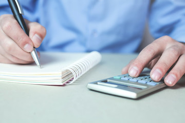 Fototapeta premium Man using calculator and writing on a notepad.