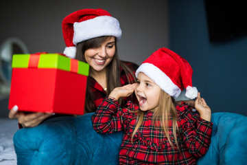 Young mother show little surprised daughter Santa's gift at home. Excited little girl surprise Christmas present in mother hands. Happy family Christmas.