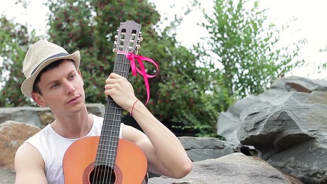 Romantic musician relaxing in nature with a guitar. The young man sitting under a tree hugging his guitar and composing the motif of a new melody