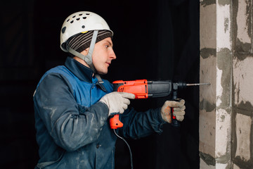 Construction worker in helmet and uniform with perforator. Man with drill