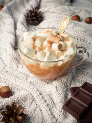 Obraz na płótnie Canvas Cozy winter home background. Cocoa in a glass Cup with a marshmallow, chocolate cinnamon cones and nuts