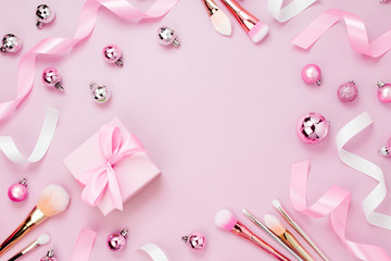 Frame with Christmas ball, gift, ribbon, cosmetic and decorations in pastel pink colour. Holiday Background. Beauty concept. Flat lay, top view