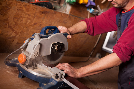 Skilled carpenter cutting a piece of wood in his woodwork workshop, using a circular saw