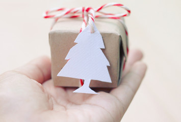 A gift wrapped in brown paper tied with red white string on hand with white paper christmas tag card.