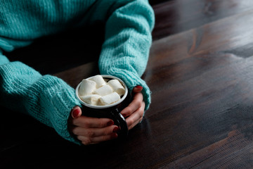 Fototapeta na wymiar girl in blue sweater holding cup of coffee with marshmallows hands close up copy space