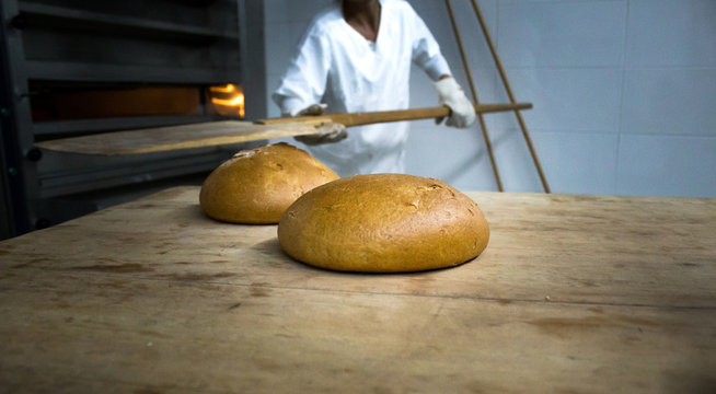 Baker woman getting bread out of bakery oven in her bakery