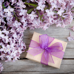 Gift box with purple bow and lilac on wood