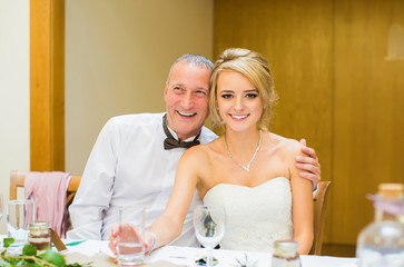 The young happy beautiful bride sitting by the table with her happy father in restaurant
