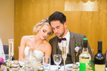 The young beautiful newlyweds sitting by the table with closed eyes in restaurant