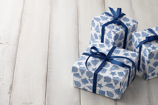 Christmas gifts or present boxes with a blue holiday print tied with ribbon on white wooden background