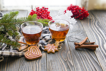 Cup of tea, fir branch, red berries, ginger cookies and cinnamon on wooden table