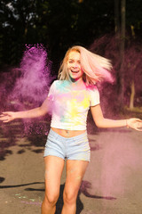 Laughing young woman in white t shirt and jeans shorts playing with pink Holi powder exploding around her