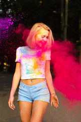 Cheerful young woman in white t shirt and jeans shorts playing with red Holi powder exploding around her
