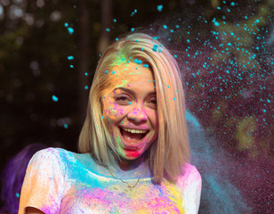 Closeup portrait of laughing young woman in white t shirt with color paint covered her face at Holi...