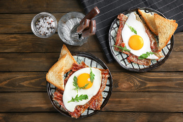 Plates with fried eggs and bacon on wooden table