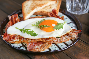 Plate with fried egg and bacon on wooden table