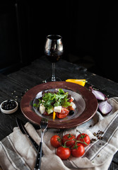 Beautifully served Greek salad with a glass of wine on a dark wooden table
