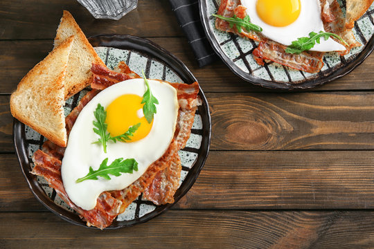 Plate with fried egg and bacon on wooden table