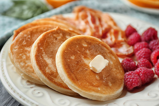 Tasty breakfast with pancakes, bacon and raspberry on plate, close up