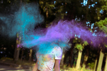 Cloud of dry colorful powder Holi exploding around young blonde woman