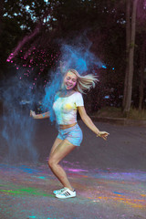 Fototapeta na wymiar Merry young woman jumping with Holi powder exploding around her