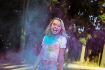 Fototapeta premium Laughing young woman with fluttering hair playing with Holi powder exploding around her