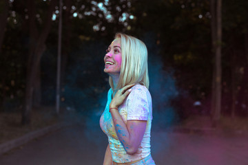 Fototapeta premium Happy blonde woman posing with Holi powder exploding around her