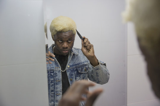 A young man using a hair pick to fix his hair in the bathroom mirror