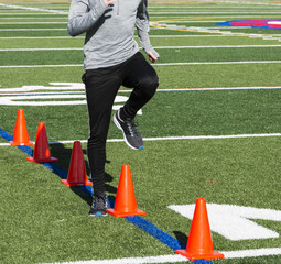 Running speed drills over orange cones on turf field