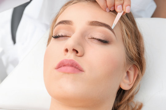 Young woman having eyebrow correction procedure in beauty salon