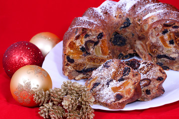 isolated traditional christmas stollen cake, sweet german bread, with dried fruits on white plate and red background with christmas decoration