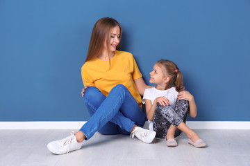 Happy mother and her daughter sitting on floor against color wall in children room