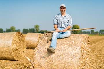 Naklejka na ściany i meble Smiling farmer sitting on hay in his field