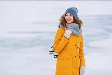 Beautiful girl in a yellow winter jacket with ice skates in the middle of a frozen lake.