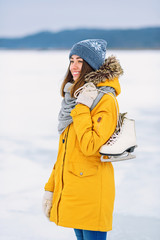 Obraz premium Beautiful girl in a yellow winter jacket with ice skates in the middle of a frozen lake.