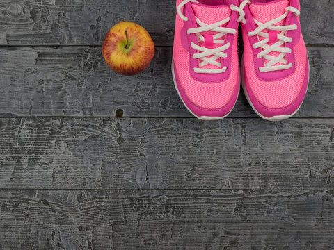 Pair pink women's running shoes for fitness and red Apple on the wooden floor. The view from the top.