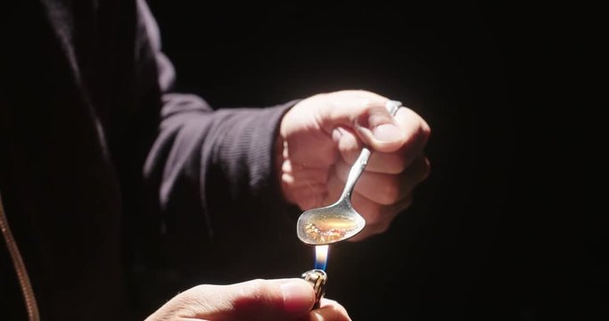 Person Holding Heroin Spoon Cooking with Lighter. a close up view of hands holding a spoon cooking heroin with a lighter side angle