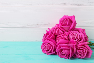 Bunch of bright pink roses flowers  on turquoise wooden background against white  wall.