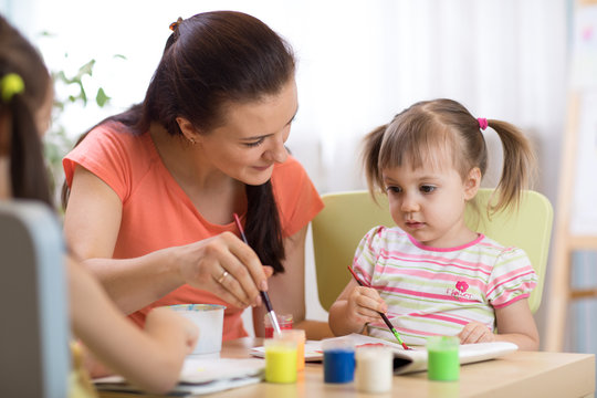 woman teaches kids painting at kindergarten or playschool