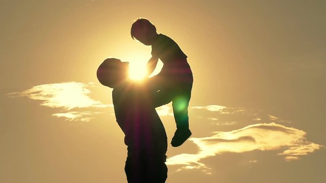 Silhouette of happy father holding on his hands and kissing his child on sunset background. The concept of a happy family at a slow pace