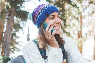 Traveling cute woman with backpack and knitted hat talking on mobile phone. Smiling. Laughing. Portrait.