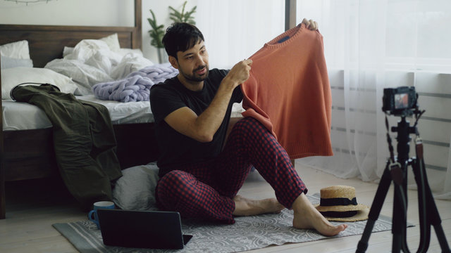 Young man fashion blogger recording video blog about clothes on camera and talking to followers at home