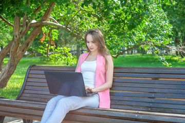 Beautiful woman sitting on a park bench using a laptop.