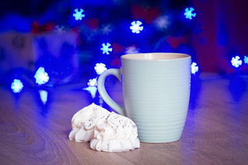 A cup of coffee with a biscuit in white chocolate, New Year / Christmas tree with red bows and blue garland on the wooden background template