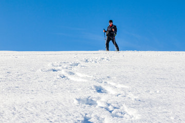 Fototapeta na wymiar Man is snowshoe hiking through deep snow on sunny day